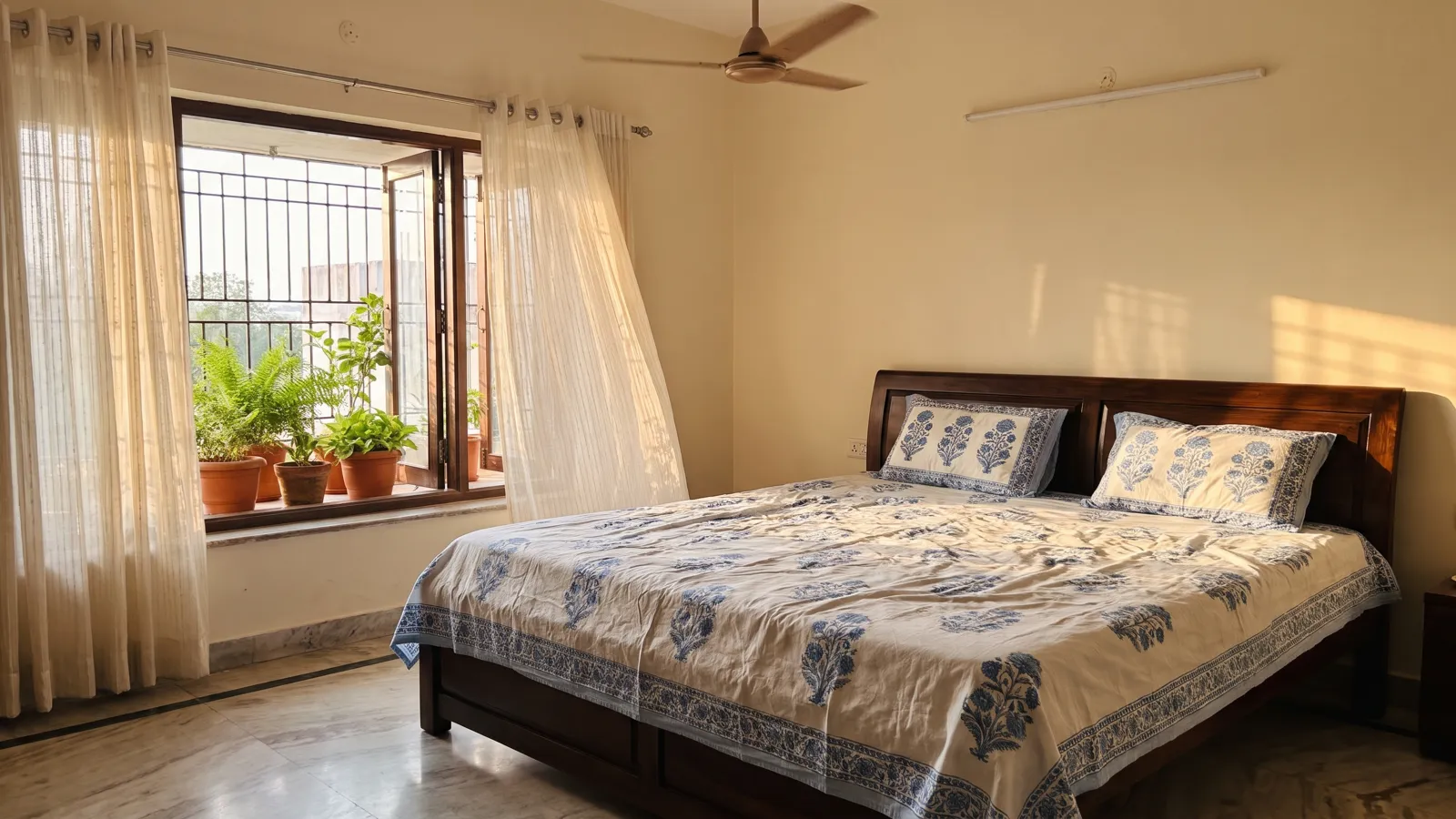 A bright Hyderabad bedroom with a blue and white block-print cotton bedsheet and sheer curtains by an open window